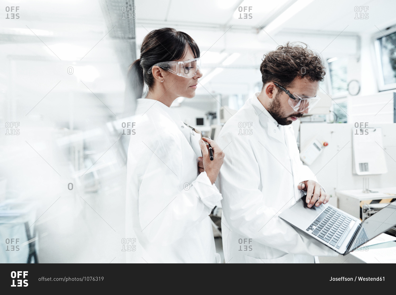 Female scientist standing by male colleague using laptop at laboratory