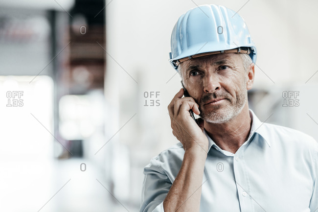 Mature male engineer in hardhat looking away while talking on mobile phone in factory