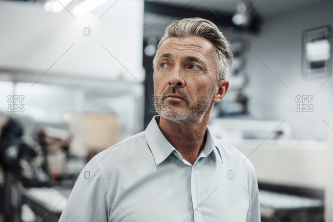 Wrinkled businessman looking away while standing in industry