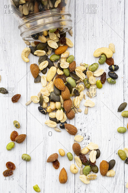 Jar of raisins- peanuts- cashew nuts- almonds- soybeans- sunflower seeds and pumpkin seeds spilled on wooden background