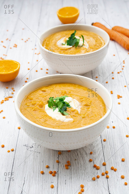 Two bowls of vegetarian lentil soup with carrots- orange juice- creme fraiche and parsley