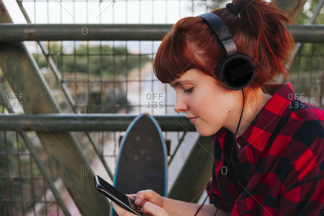 Redhead woman text messaging while listening music through headphones