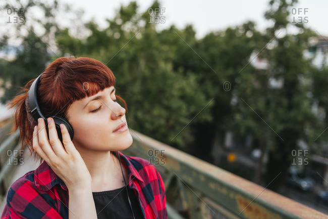 Redhead woman with eyes closed listening music through headphones