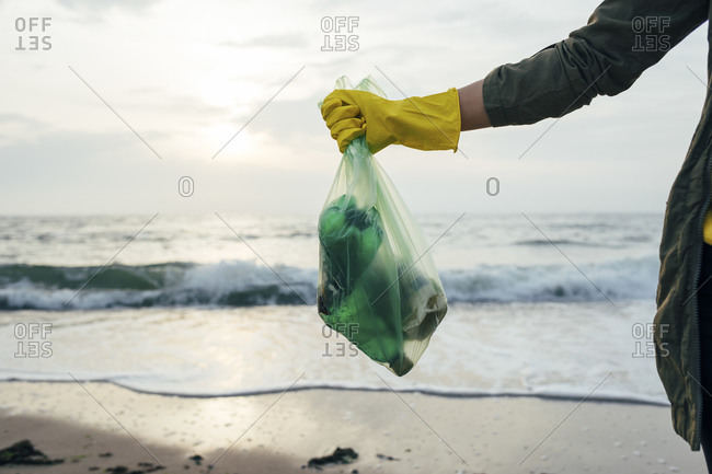 Mid adult woman holding garbage bag while standing at beach