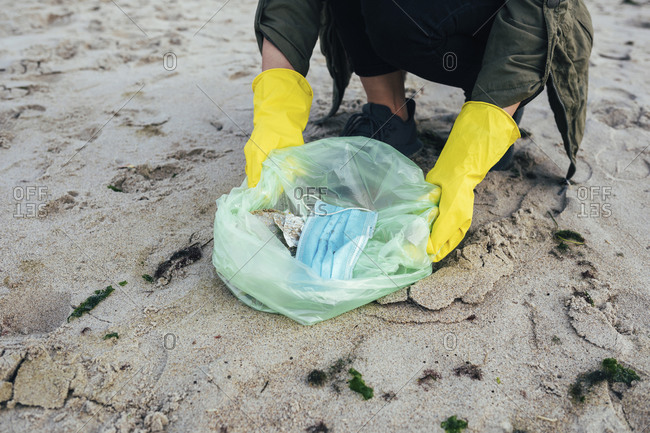 Woman collecting disposable face mask in garbage bag while cleaning beach