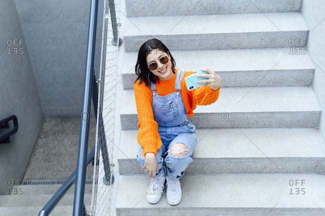 Young woman smiling while taking selfie through smart phone sitting on staircase