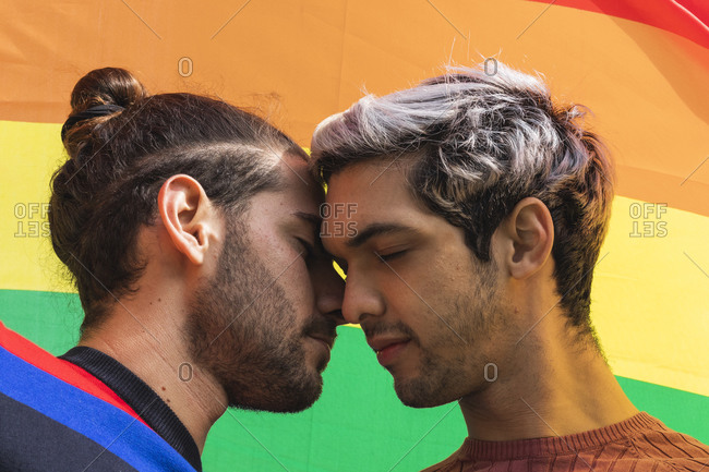 Affectionate man flirting with male partner against rainbow scarf