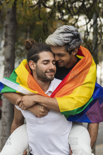 Affectionate man with rainbow scarf embracing male partner against tree