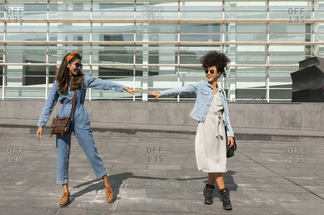 Smiling female friends stretching hand towards each other while standing on rooftop