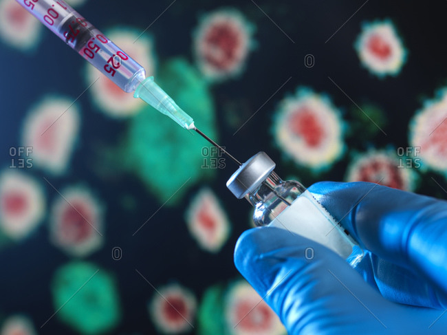 Scientist drawing out a vaccine from a vial with a virus on the computer screen in the background.