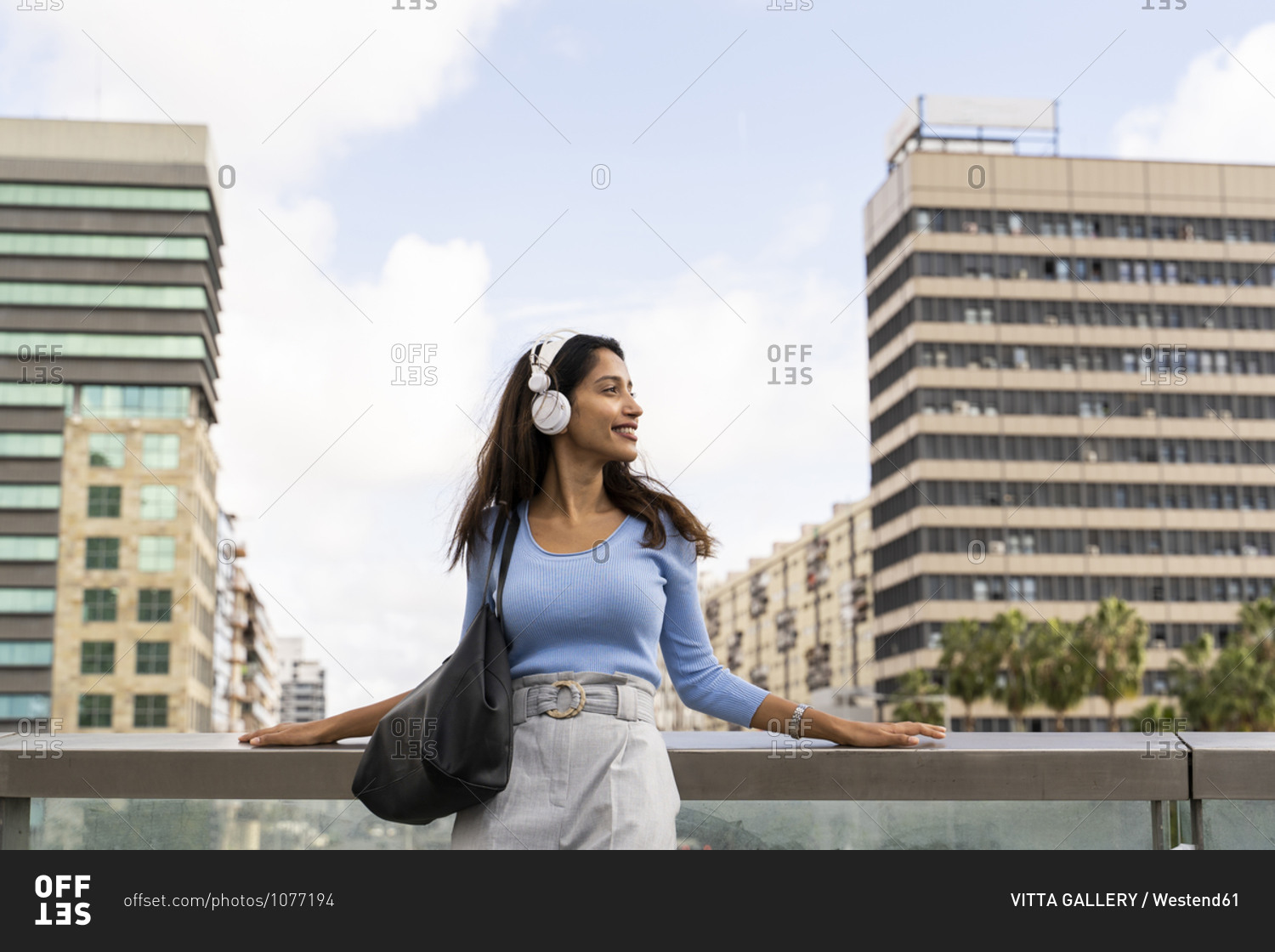 Beautiful young businesswoman listening music through headphones while leaning on railing