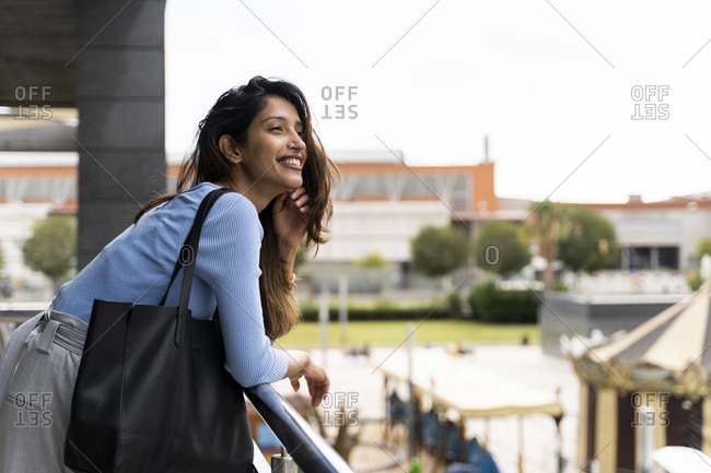 Smiling woman with purse leaning on railing in city