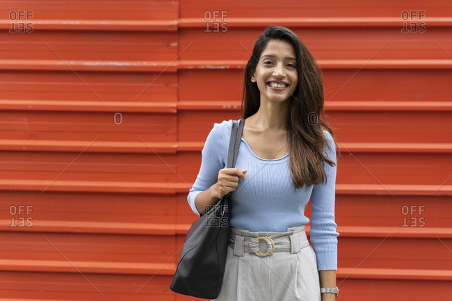 Smiling confident woman with purse standing against shutter