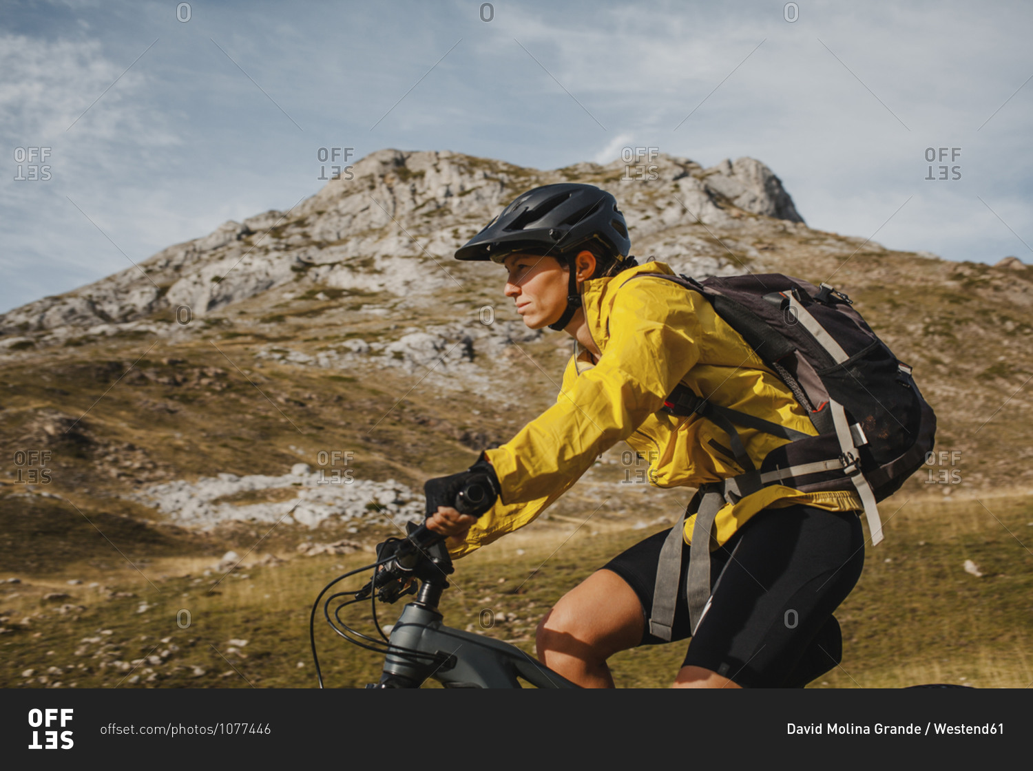 Mid adult woman with backpack riding electric bicycle on mountain at Somiedo Natural Park- Spain