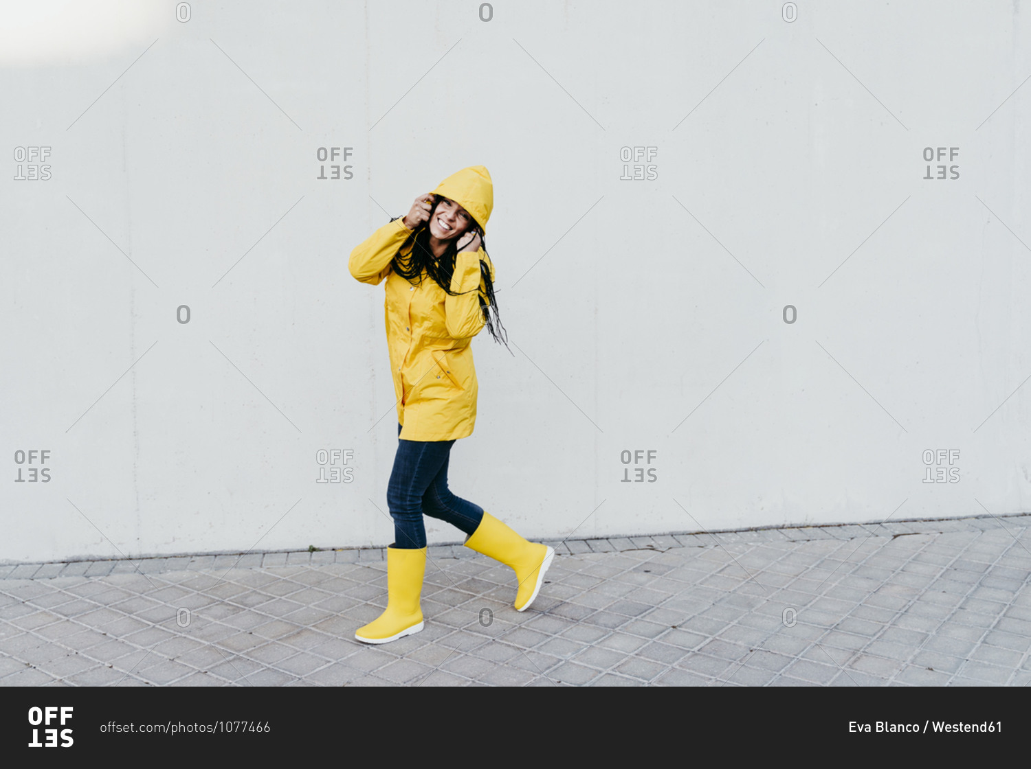 Smiling woman wearing raincoat standing on footpath against gray wall