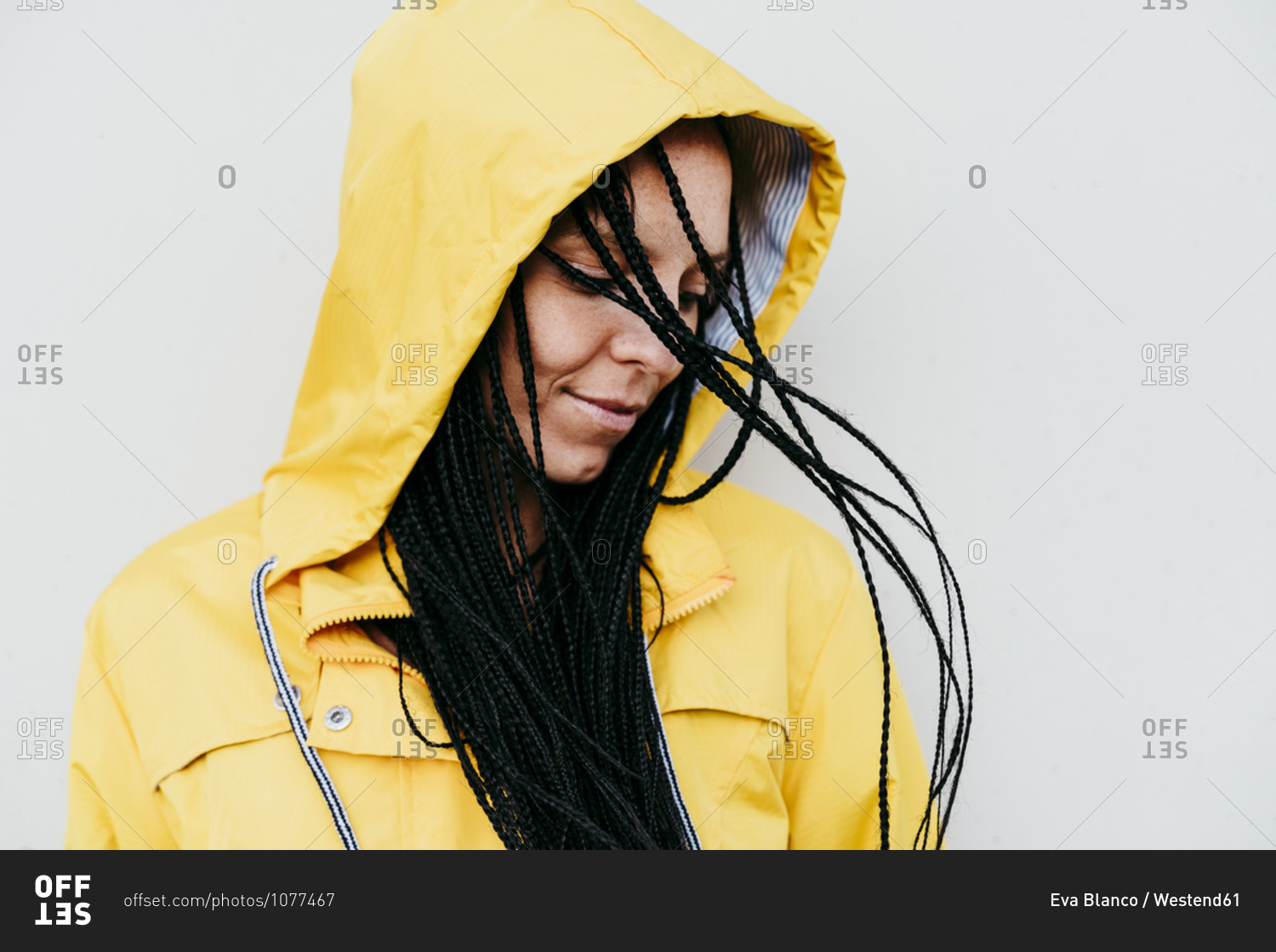 Woman wearing raincoat looking down against gray wall