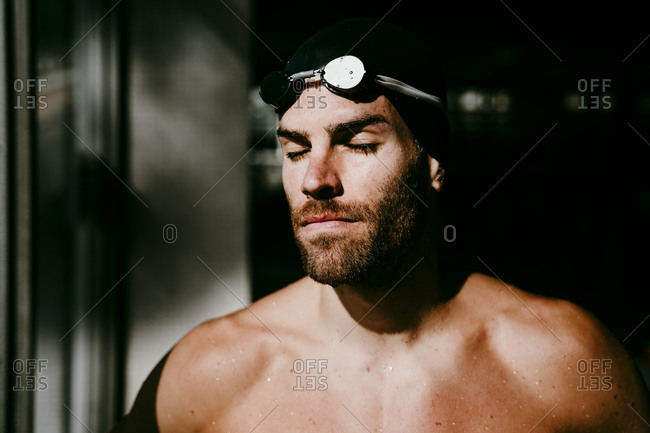 Shirtless male swimmer with eyes closed by window