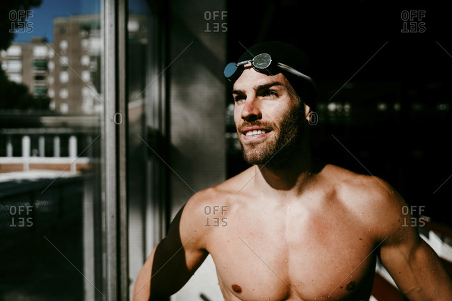 Smiling shirtless male swimmer standing by window