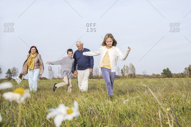 Grandparents with grandchildren spending leisure time on field against sky during weekend
