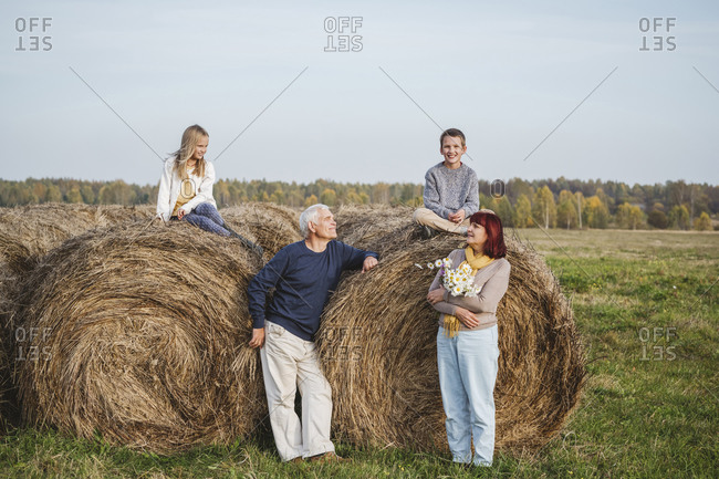 Senior couple with grandchildren sitting on hay bales on field during weekend