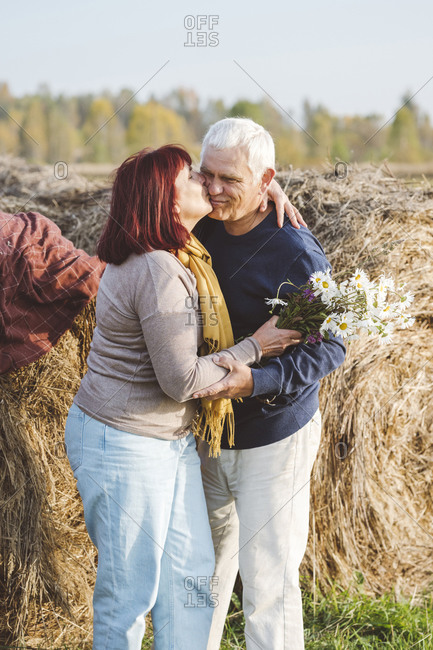 Happy senior couple kissing while standing against hay bales at field
