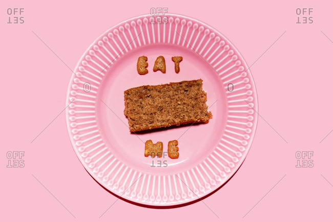 Slice of cake on pink plate with message Eat Me made of biscuit letters