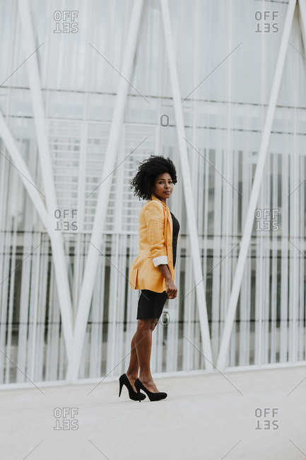 Businesswoman wearing orange blazer standing on footpath against building