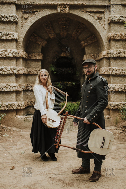 Male and female holding lyra musical instrument against built structure