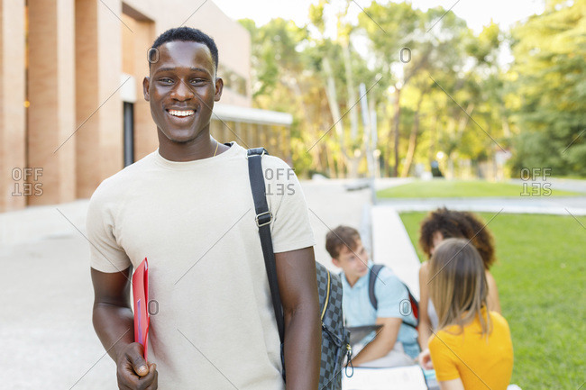 Smiling confident male student with folder standing in university campus