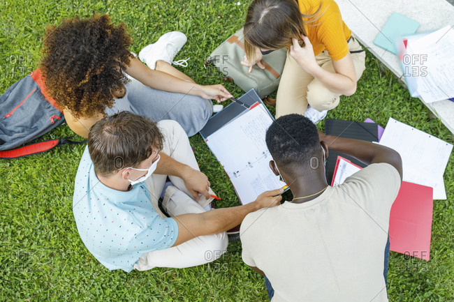 Students sitting on grass while studying together in university campus