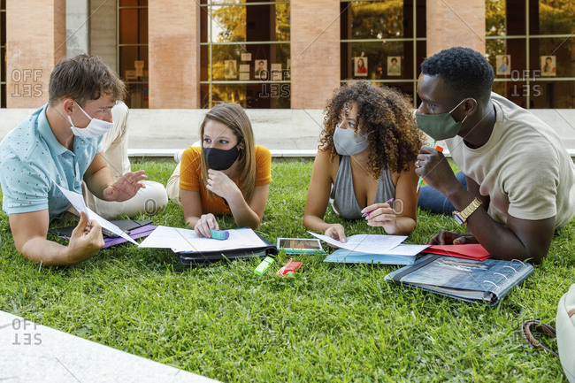 Male and female students wearing safety mask while discussing on grass in university campus