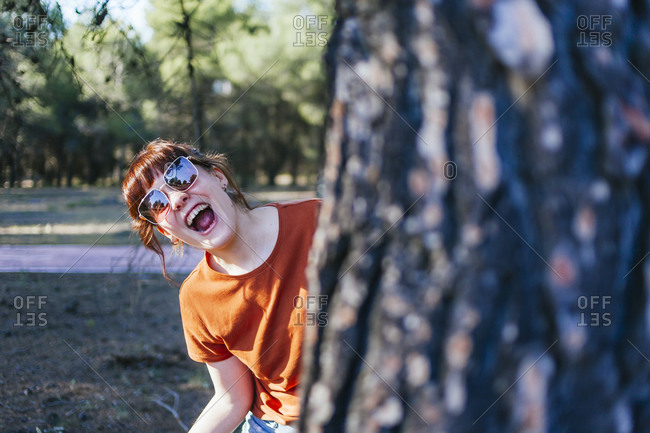 Young woman laughing while peeking from tree