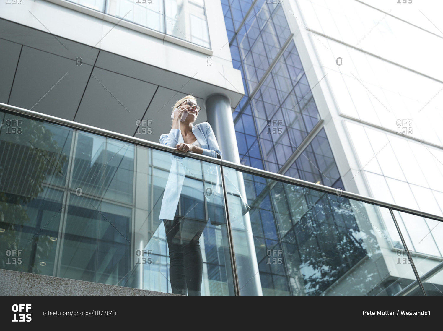 Woman talking on mobile phone while leaning on railing against building