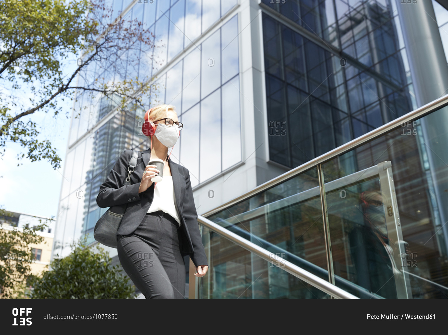 Woman wearing face mask listening music while walking against building