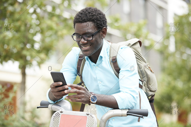 Smiling man text messaging on smart phone while leaning on bicycle