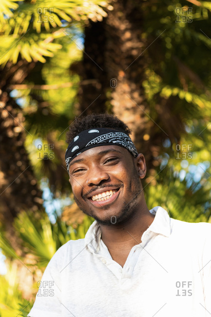 Cheerful young man wearing headscarf against palm tree