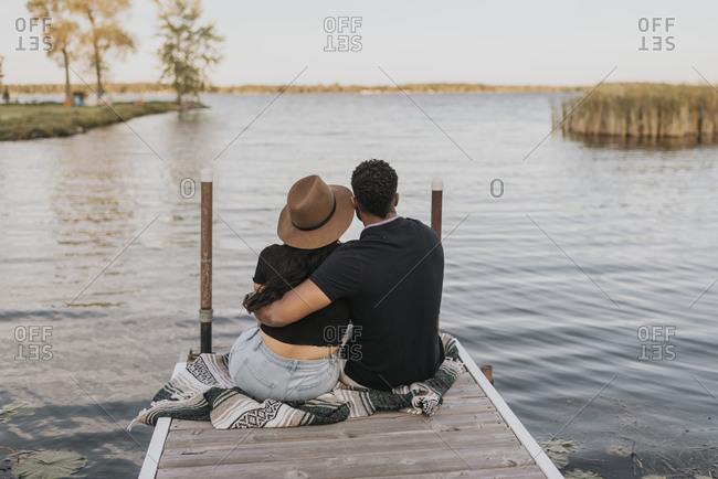 Couple with arm around admiring view while sitting on pier against lake
