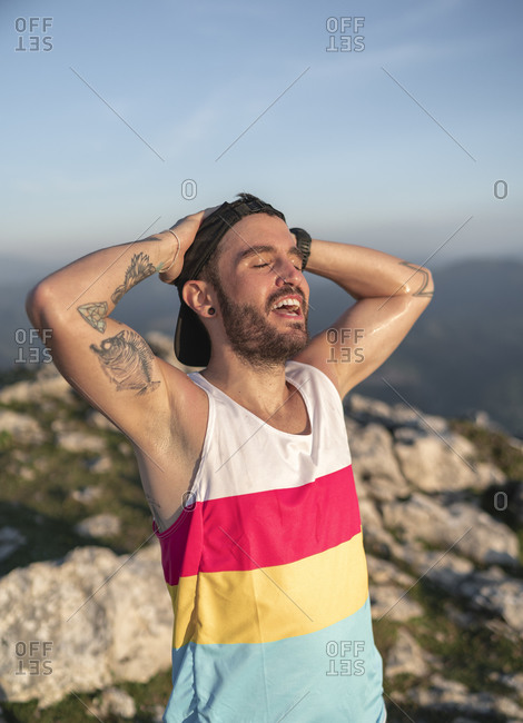 Smiling man with hands behind head standing on mountain against clears sky