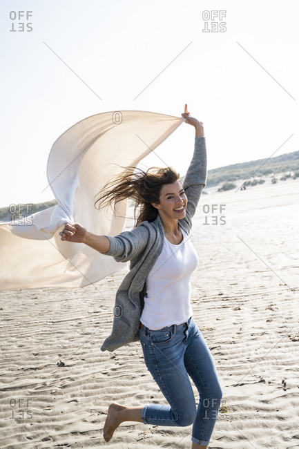 Cheerful woman running while holding blanket at beach on sunny day