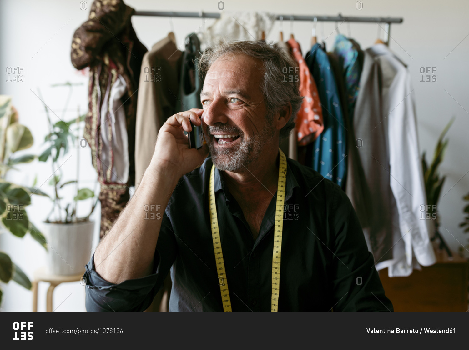 Happy male costume designer looking away while talking on mobile phone at work studio