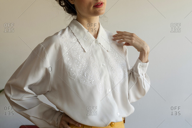 Woman wearing white shirt with hand on hip standing against wall