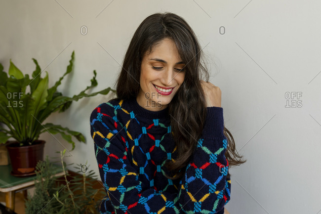 Smiling female model with hand in hair sitting at home