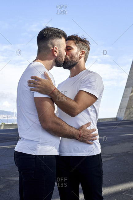 Affectionate gay couple kissing on bridge against sky