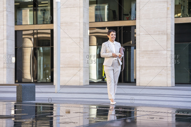 Businesswoman holding purse while standing by fountain in city