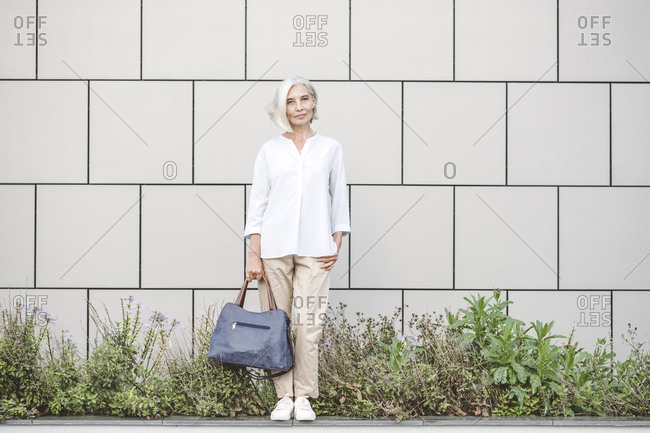 Businesswoman holding purse while standing against wall