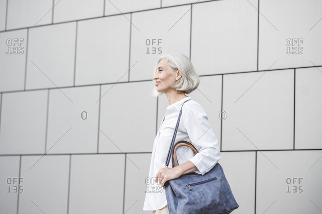 Smiling businesswoman with purse looking away while standing against wall