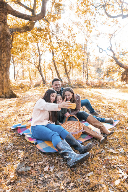 Family taking selfie on smart phone while sitting in park during autumn