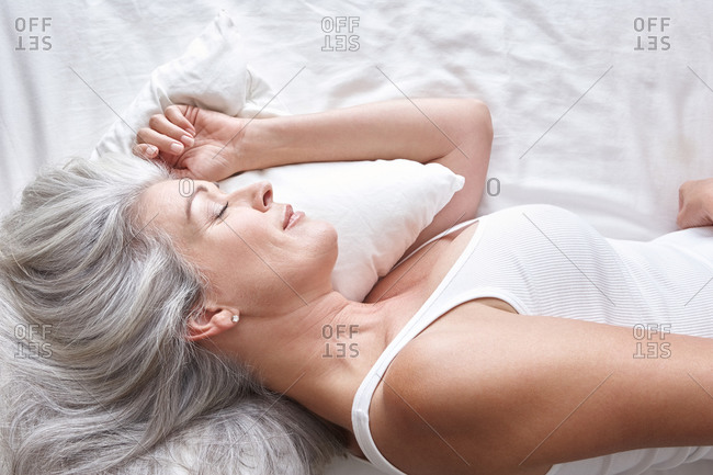 Mature attractive Caucasian woman sleeping on white sheets