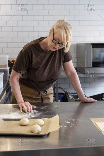 Woman in brown apron standing in a cafe kitchen, mixing baking danish pastry dough