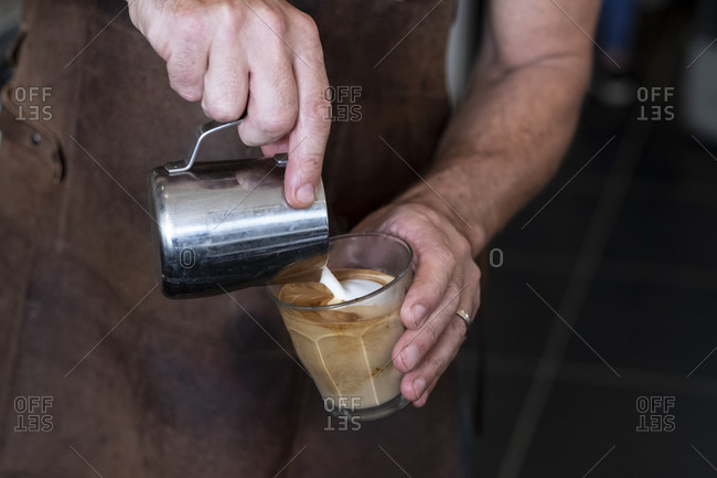 Close up of barista wearing brown apron pouring cafe latte.